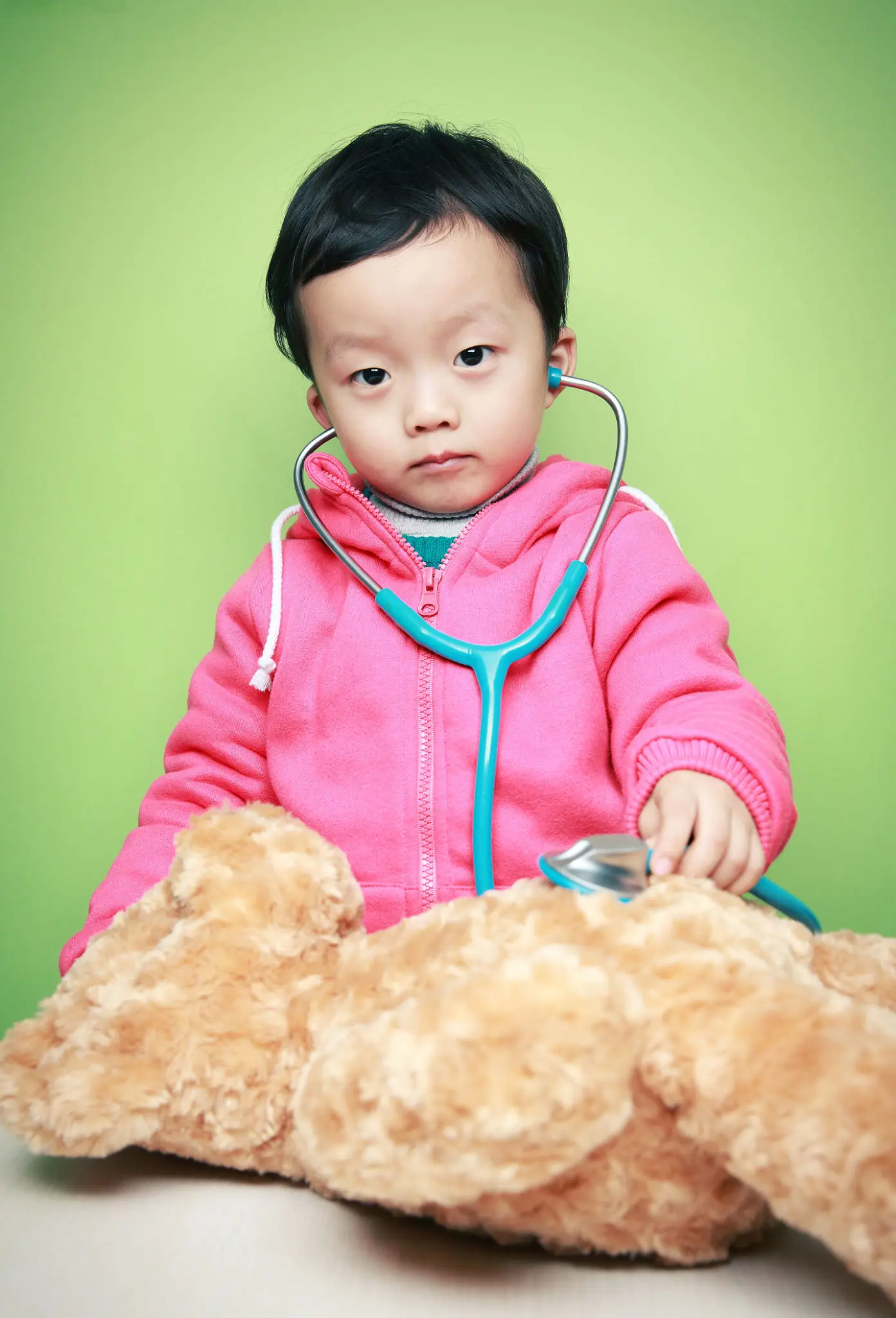 Child with stethoscope examining teddy bear.