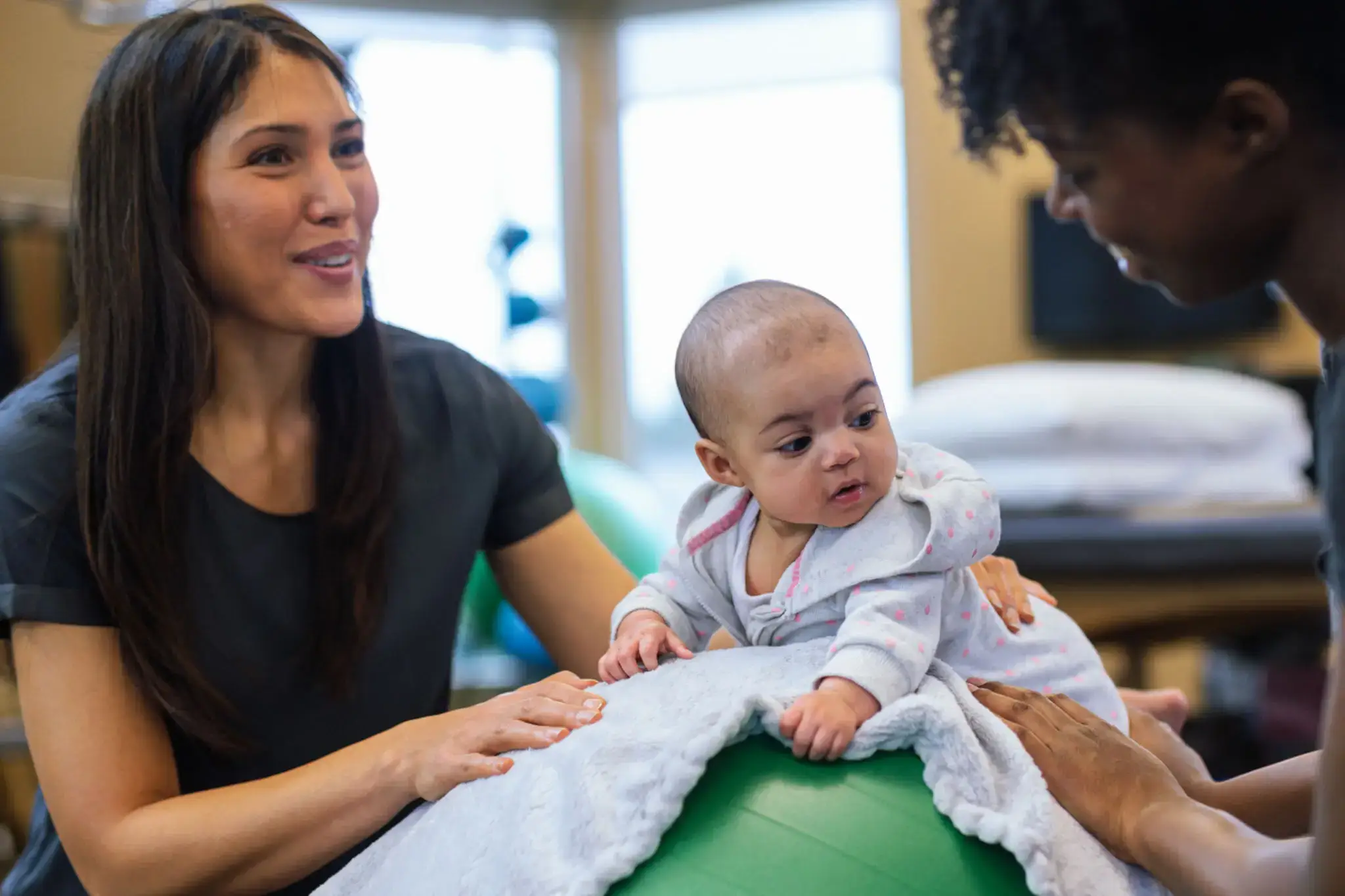 Baby on exercise ball with two adults.