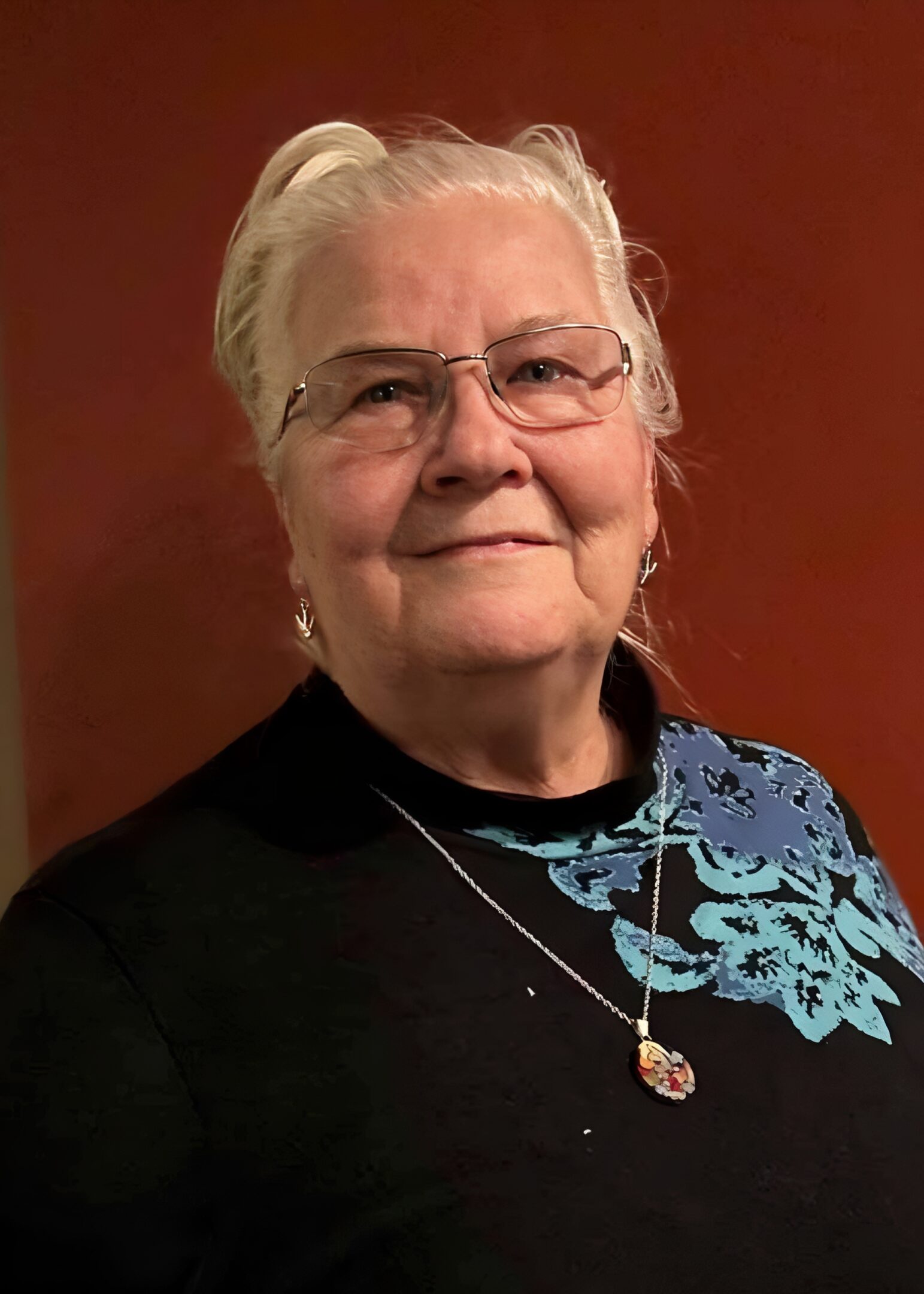 Elderly woman smiling with glasses and necklace.